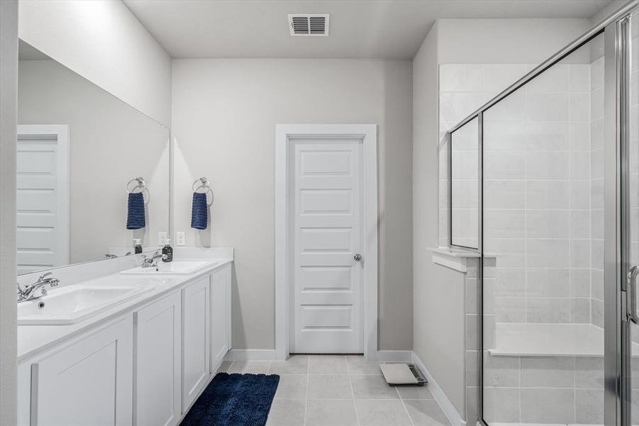 Bathroom with a shower with shower door, tile flooring, and double sink vanity