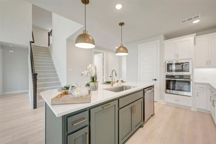 Kitchen island featuring a single-basin sink with a gold-tone faucet, white countertop, and deep green cabinetry
