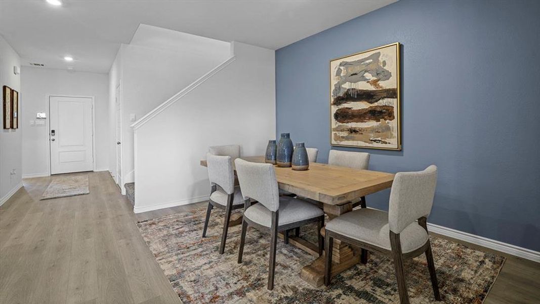 Open concept living space featuring wood-finish flooring, a neutral color palette, and a staircase with white risers and handrails Open concept living space featuring wood-finish flooring, a neutral color palette, and a staircase with white risers and handrails