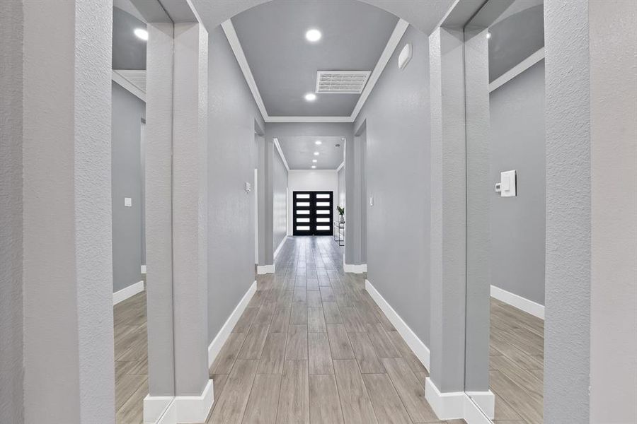 Hallway with light wood-finish flooring, recessed lighting, crown molding, and a modern paneled entryway door