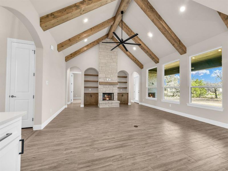 Unfurnished living room with a fireplace, light hardwood / wood-style floors, ceiling fan, and beamed ceiling