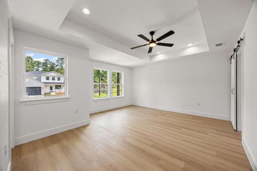 Empty room featuring a tray ceiling, a barn door, light wood-type flooring, a ceiling fan, and recessed lighting Empty room featuring a tray ceiling, a barn door, light wood-type flooring, a ceiling fan, and recessed lighting