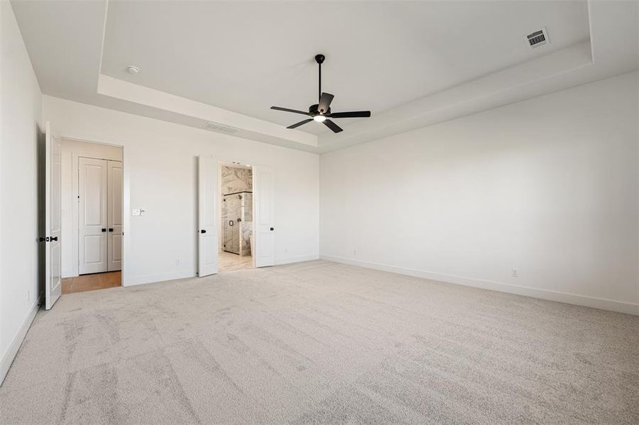 Unfurnished bedroom with a tray ceiling, light carpet, a ceiling fan, and connected bathroom
