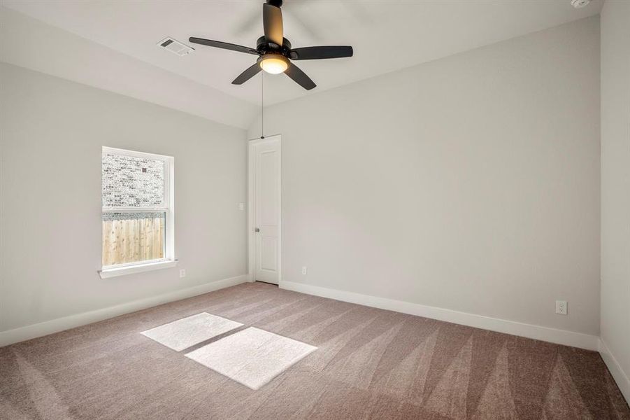 This bright and airy secondary bedroom invites endless possibilities, featuring elegant sloped ceilings and a modern ceiling fan to keep the atmosphere cool and breezy.