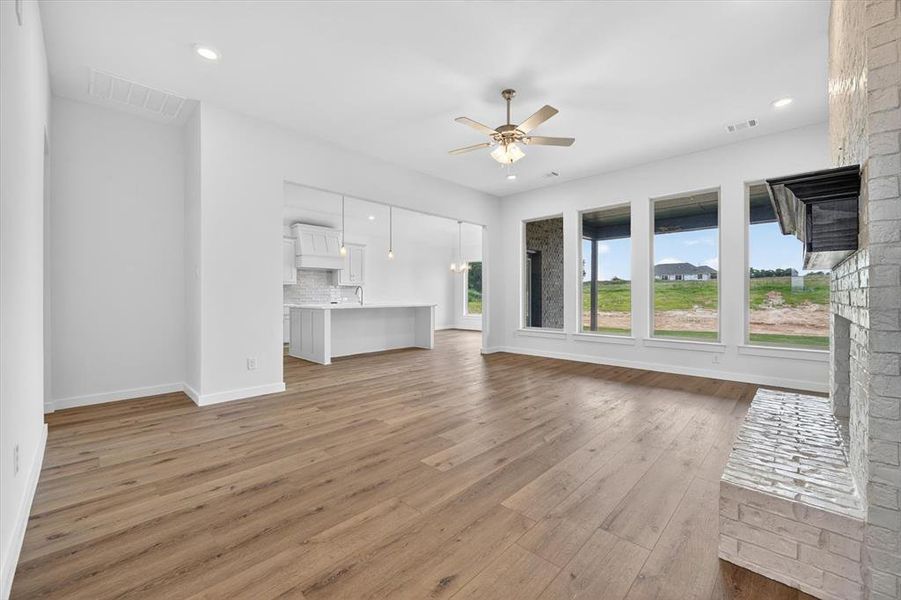 Open-concept living area featuring wood-finish flooring, a stone-clad fireplace, and a ceiling fan with integrated lighting
