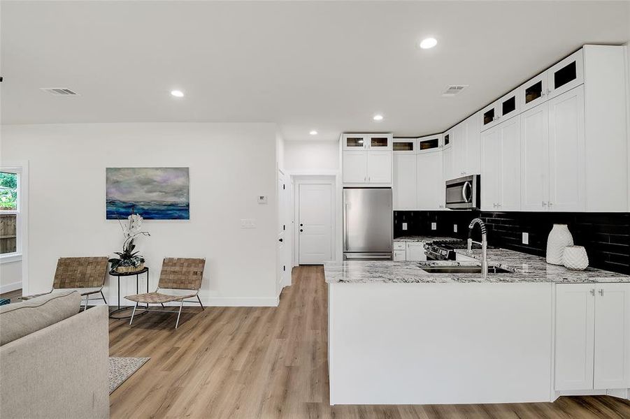 Kitchen with wood-style flooring, sink, light granite countertops, appliances with stainless steel finishes, and white cabinetry