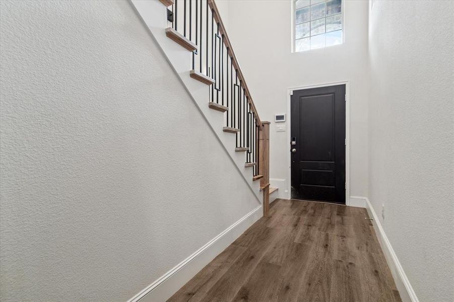 Foyer entrance featuring dark wood-style floors, stairs, a textured wall, and a high ceiling Foyer entrance featuring dark wood-style floors, stairs, a textured wall, and a high ceiling