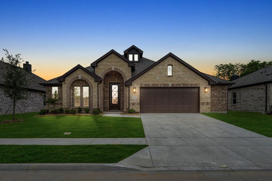 Single-story home with stone and brick exterior, arched entry, two-car garage, and green lawn at dusk