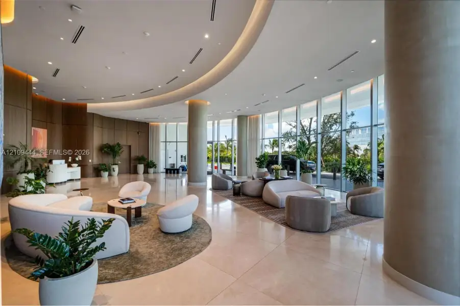 Expansive lobby featuring floor-to-ceiling glass walls, polished stone flooring, custom curved recessed ceiling lighting, and wood-paneled walls