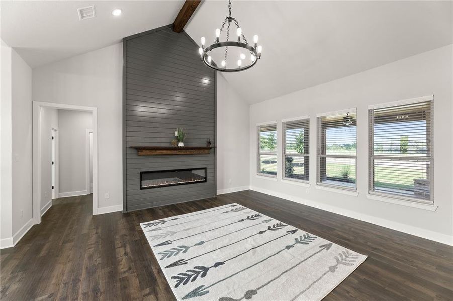 Living area featuring high vaulted ceiling, beamed ceiling, a chandelier, dark wood-style floors, and a large fireplace Living area featuring high vaulted ceiling, beamed ceiling, a chandelier, dark wood-style floors, and a large fireplace
