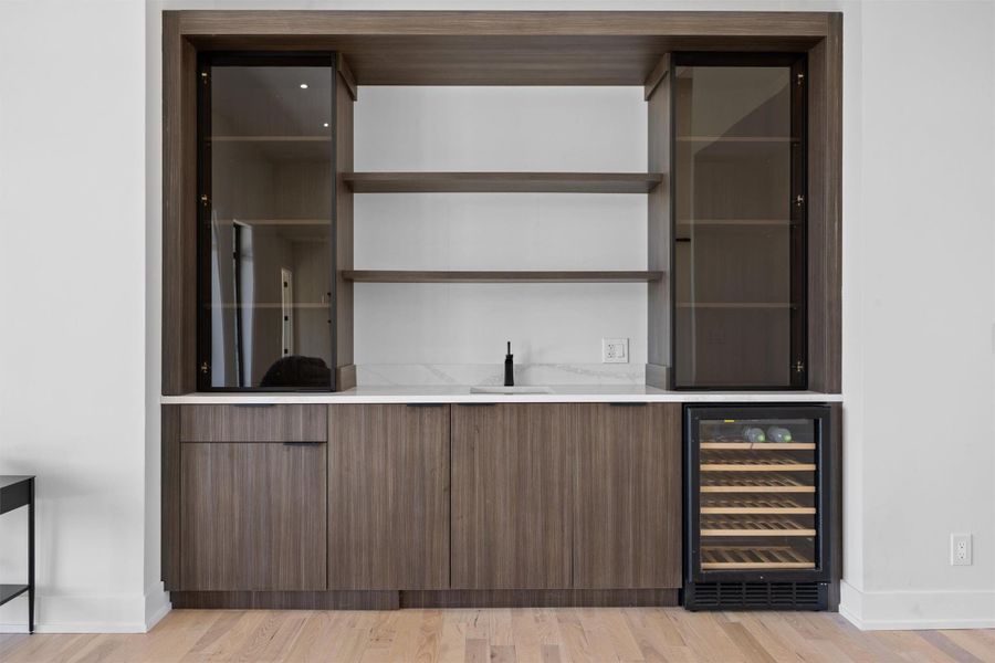 Bar featuring beverage cooler, baseboards, light wood finished floors, wet bar, and a sink