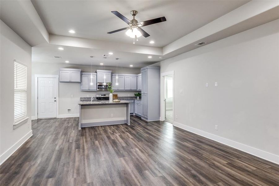 Kitchen featuring a kitchen island, open floor plan, a raised ceiling, dark wood-type flooring, and recessed lighting