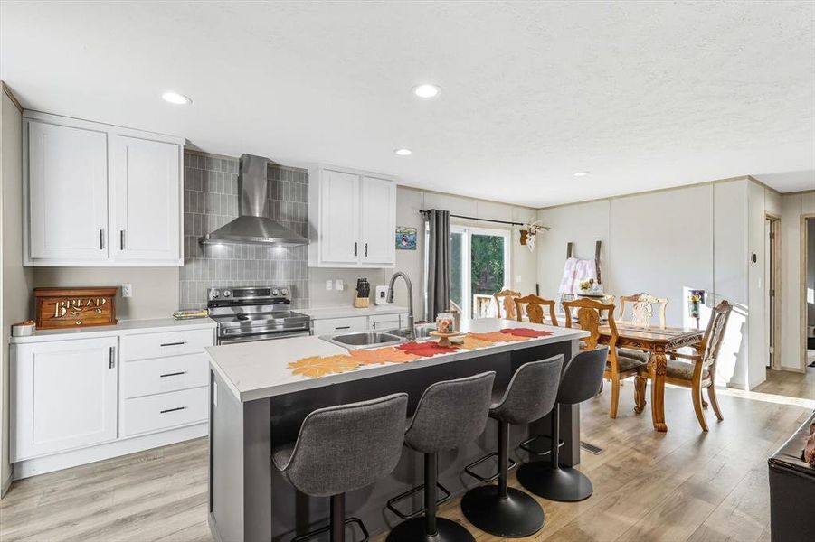 Kitchen featuring wall chimney range hood, light wood finished floors, electric range, light countertops, and recessed lighting Kitchen featuring wall chimney range hood, light wood finished floors, electric range, light countertops, and recessed lighting