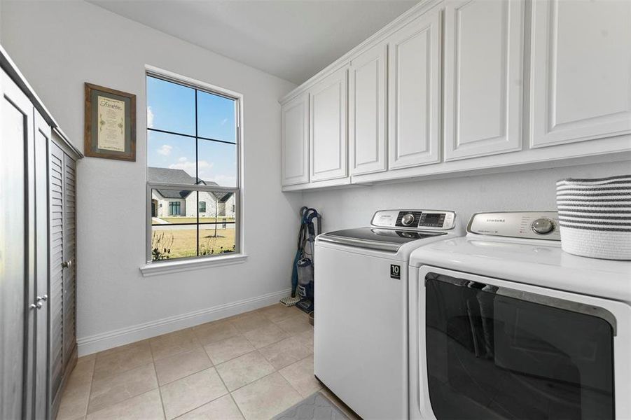 Washroom featuring washing machine and clothes dryer, light tile patterned floors, and cabinets