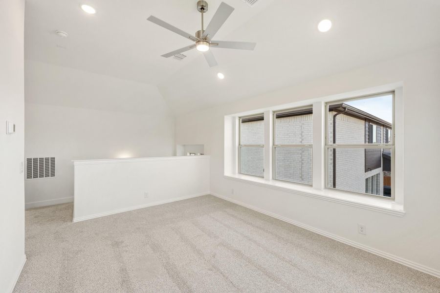 Empty bedroom with vaulted ceiling, ceiling fan, carpet flooring, and large windows