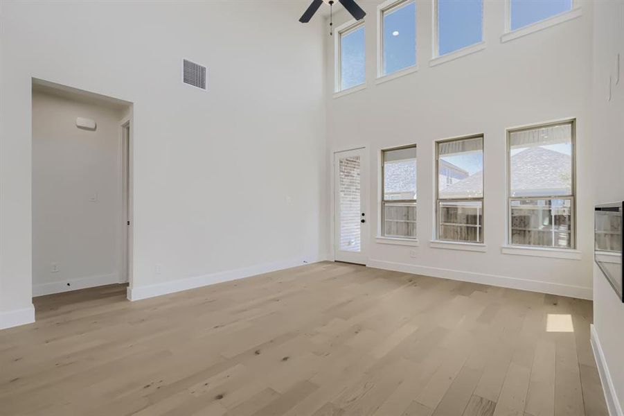 Two-story living area featuring wood-finish flooring, a contemporary ceiling fan, and a wall of windows