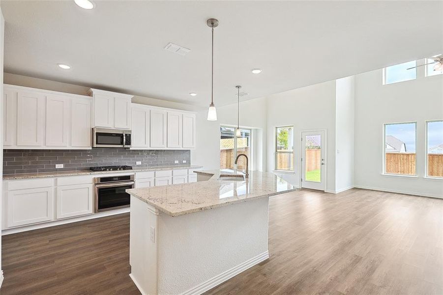 Kitchen featuring white cabinets, pendant lighting, stainless steel appliances, and a kitchen island with sink