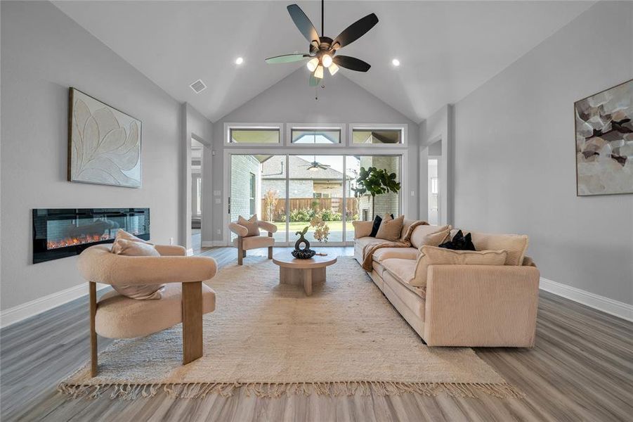 Living area featuring a glass covered fireplace, high vaulted ceiling, wood finished floors, ceiling fan, and recessed lighting Living area featuring a glass covered fireplace, high vaulted ceiling, wood finished floors, ceiling fan, and recessed lighting