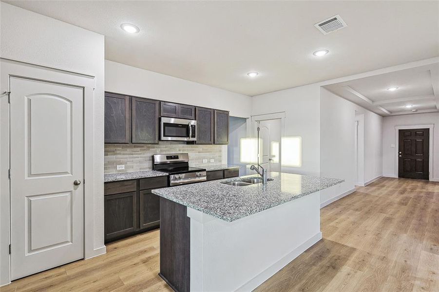 Kitchen featuring light hardwood / wood-style floors, appliances with stainless steel finishes, a center island with sink, and sink