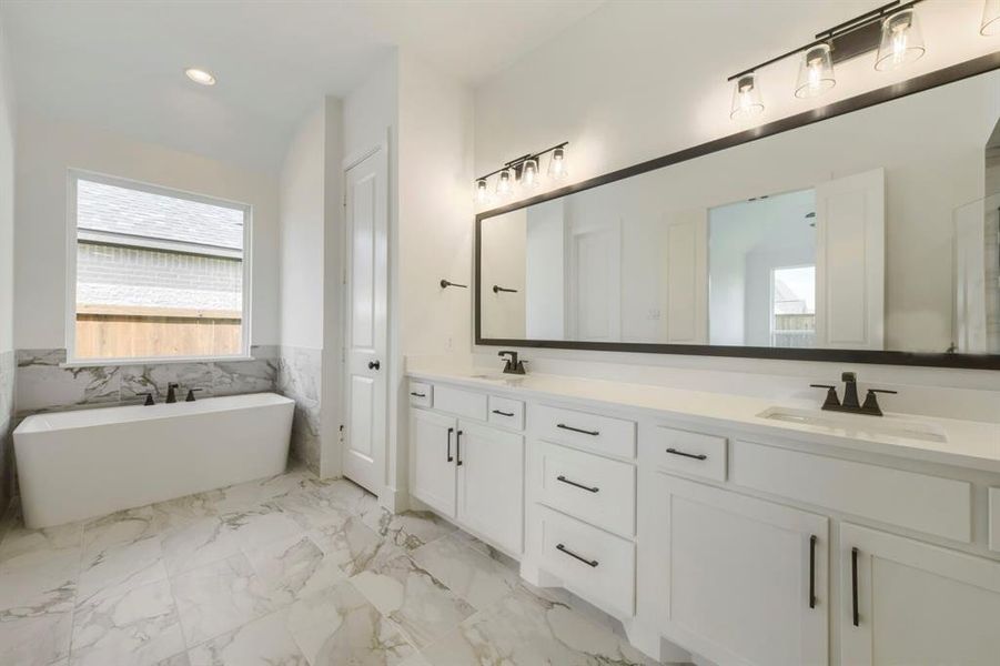Freestanding soaking tub with dark-finish hardware, set against a window and marble-patterned tile wainscoting Freestanding soaking tub with dark-finish hardware, set against a window and marble-patterned tile wainscoting