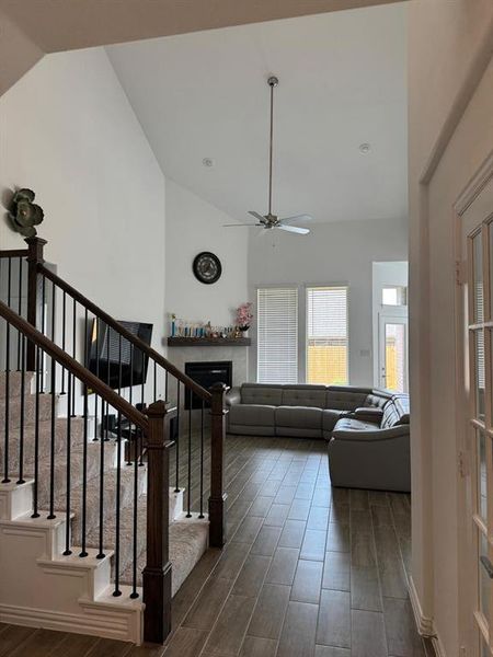 Entry foyer featuring wood-finish tile flooring, a carpeted staircase with dark wood newel posts and black iron balusters, and an open layout to the living area Entry foyer featuring wood-finish tile flooring, a carpeted staircase with dark wood newel posts and black iron balusters, and an open layout to the living area