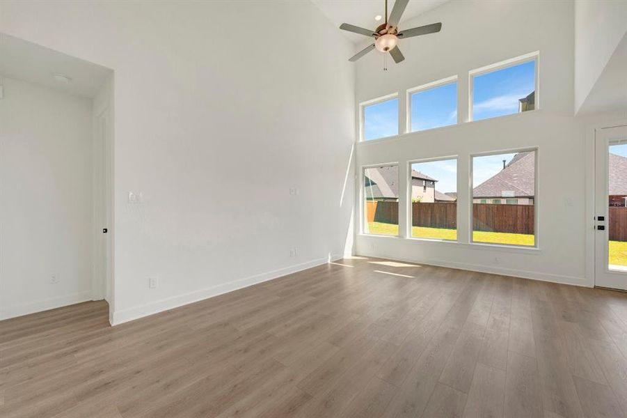 Two-story living area featuring wood-finish flooring, a contemporary ceiling fan, and a wall of windows with transom panels
