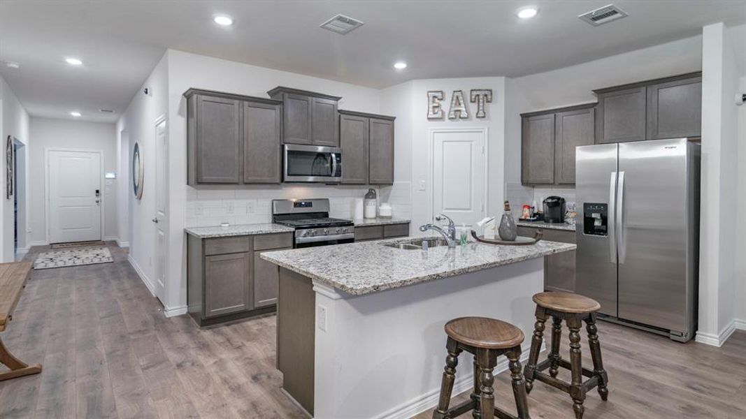 Kitchen featuring appliances with stainless steel finishes, light stone counters, light wood-type flooring, backsplash, and an island with sink Kitchen featuring appliances with stainless steel finishes, light stone counters, light wood-type flooring, backsplash, and an island with sink