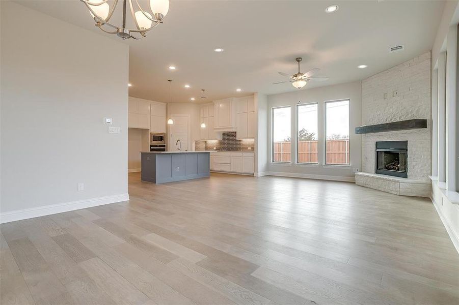 Unfurnished living room with ceiling fan with notable chandelier, a stone fireplace, and light wood-type flooring