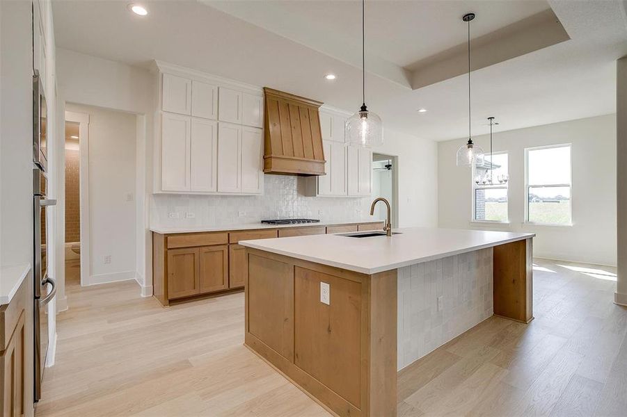 Kitchen with sink, light wood-type flooring, hanging light fixtures, white cabinets, and a center island with sink