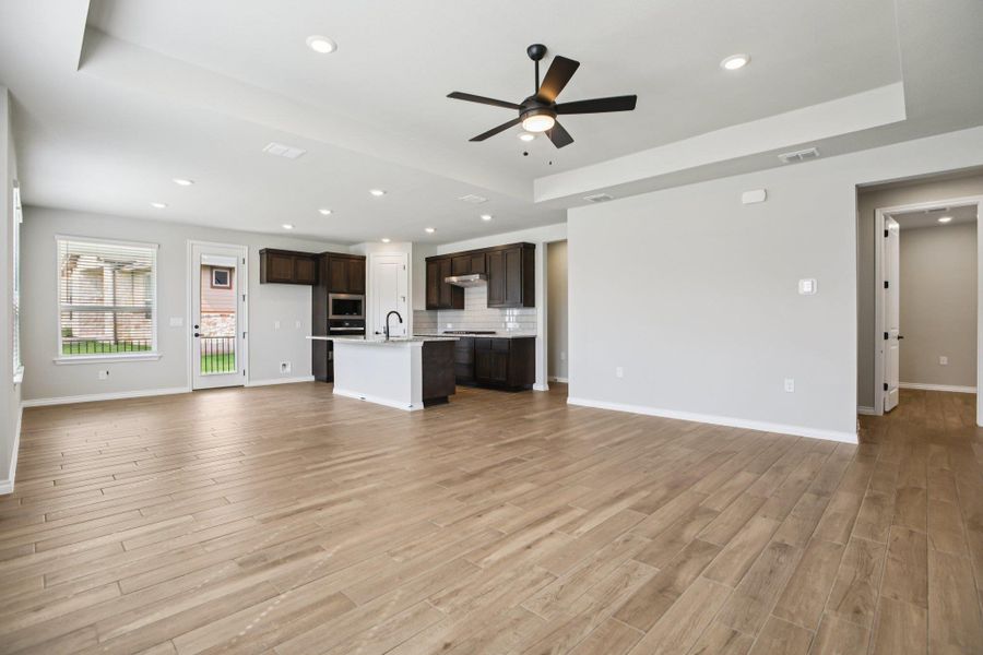 Unfurnished living room featuring a tray ceiling, a ceiling fan, recessed lighting, and light wood-type flooring Unfurnished living room featuring a tray ceiling, a ceiling fan, recessed lighting, and light wood-type flooring