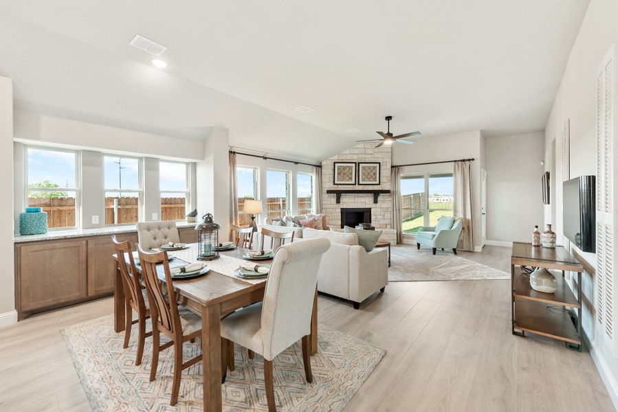 Open-concept dining and living area with stone fireplace, ceiling fan, and light wood floors Open-concept dining and living area with stone fireplace, ceiling fan, and light wood floors