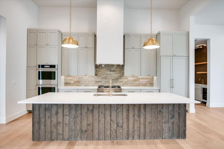 Kitchen featuring a large center island with a wood-finish plank base, light stone countertop, and integrated sink