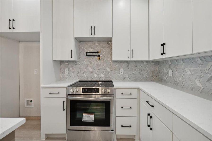 Kitchen featuring white cabinetry, light stone counters, stainless steel electric range oven, and backsplash