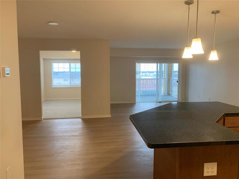 Entering the unit you will se kitchen with dark countertops, open floor plan, pendant lighting, dark wood-style floors, and a kitchen island