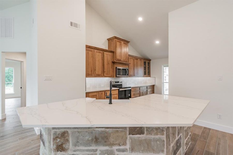 Kitchen featuring stainless steel appliances, light wood-style floors, decorative backsplash, brown cabinetry, and high vaulted ceiling