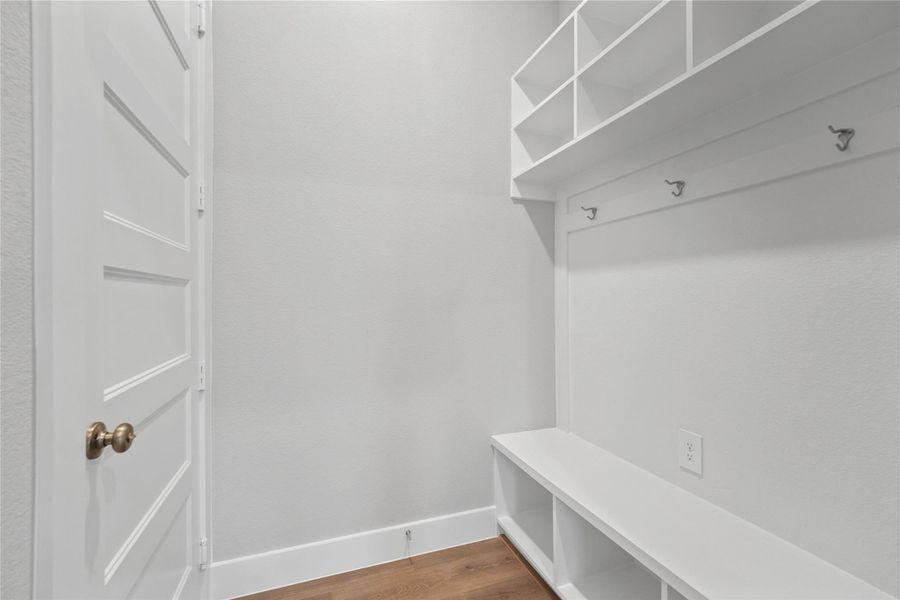 Step into this highly functional and stylish mudroom drop zone, an essential feature for a busy household. The space boasts custom-built white cabinetry and shelving, providing generous storage for coats, bags, and shoes. A comfortable built-in bench offers a convenient spot to sit, while three sleek hooks keep outerwear tidy and accessible.