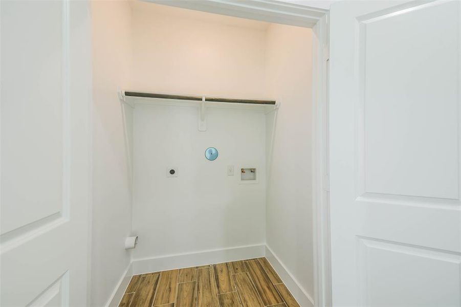 You're looking at a compact laundry closet with built-in connections, a shelf for storage, and wood flooring, all enclosed by a clean, white door. Ideal for efficient space utilization in a modern home.