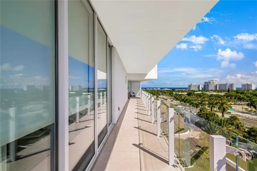 Covered balcony featuring expansive floor-to-ceiling glass doors, tile flooring, and a frameless glass railing Covered balcony featuring expansive floor-to-ceiling glass doors, tile flooring, and a frameless glass railing