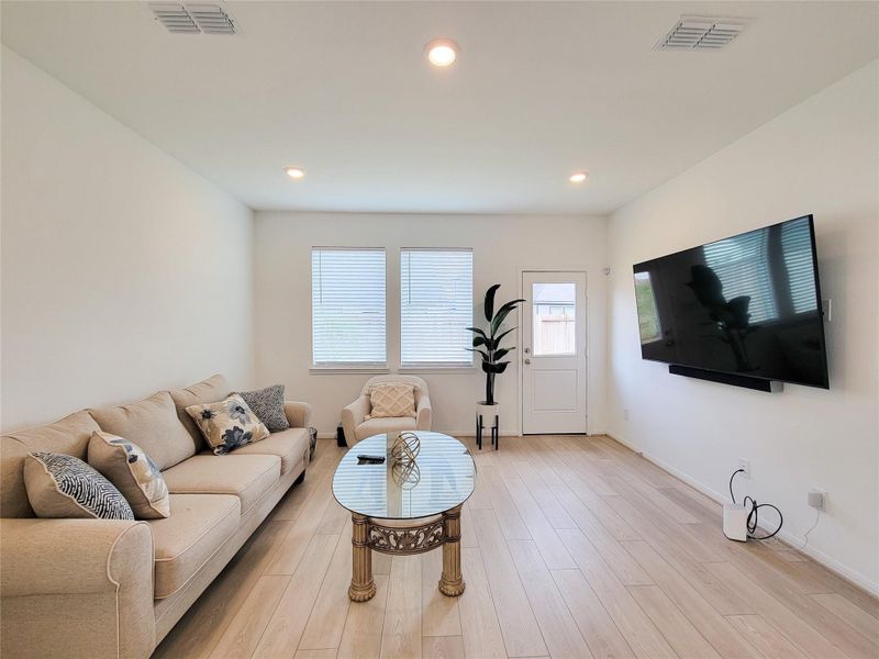 Bright and modern living room with light wood flooring, neutral walls, and recessed lighting.