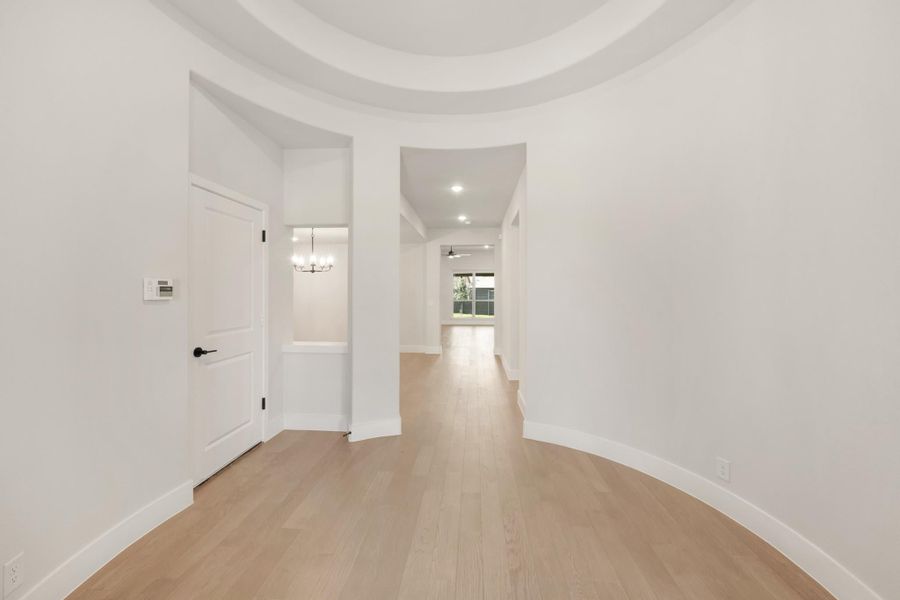Curved entryway with round tray ceiling, light hardwood floors, and open hallway leading to main living areas