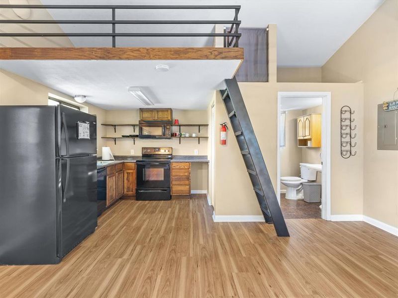 Kitchen featuring black appliances, open shelves, light wood finished floors, electric panel, and brown cabinets Kitchen featuring black appliances, open shelves, light wood finished floors, electric panel, and brown cabinets