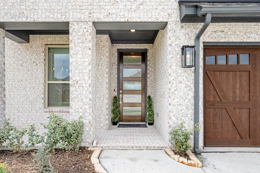 Home entrance with wood and glass front door, white brick exterior, and wood garage door nearby