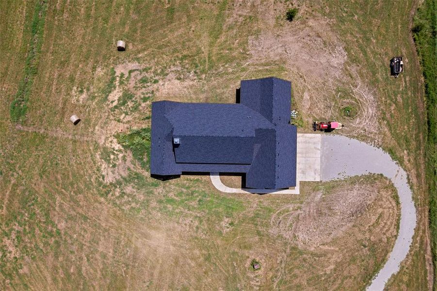New construction residence featuring a dark shingle roof, a concrete driveway, and an expansive gravel access path