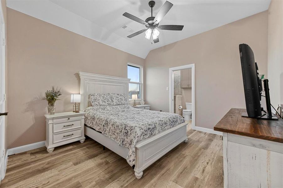 Bedroom featuring light wood-type flooring, ensuite bath, ceiling fan, and lofted ceiling