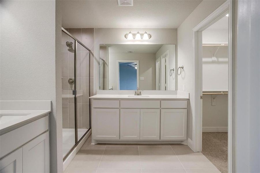 Full bathroom featuring a stall shower, two vanities, light tile patterned floors, and a spacious closet Full bathroom featuring a stall shower, two vanities, light tile patterned floors, and a spacious closet