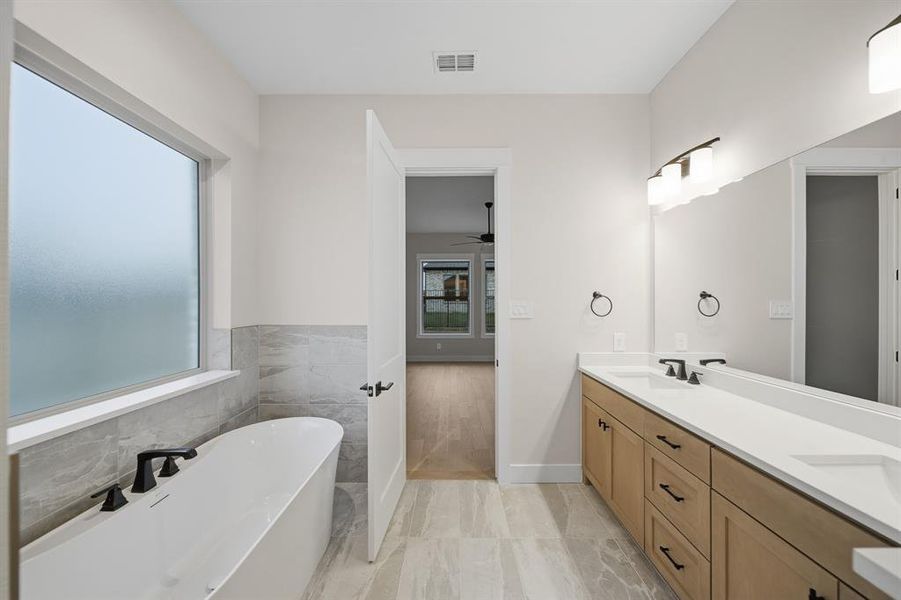 Full bathroom featuring a soaking tub, double vanity, tile walls, and a ceiling fan
