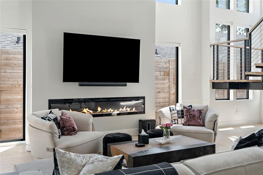 Living room with fireplace, grand stairway, light wood flooring, and custom electric shades