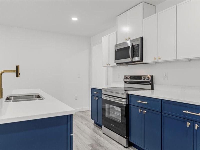 Kitchen featuring blue cabinets, appliances with stainless steel finishes, light wood-style flooring, white cabinetry, and recessed lighting