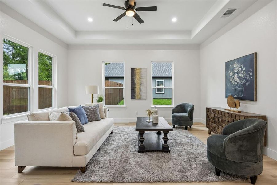 Bright living area featuring a tray ceiling with recessed lighting and a ceiling fan and multiple windows