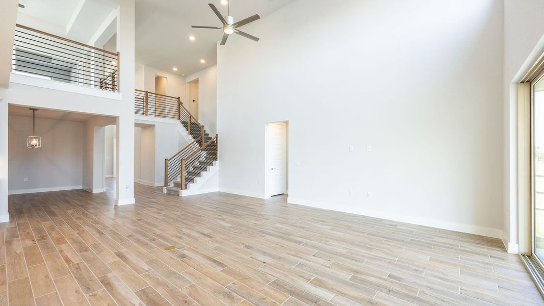 Unfurnished living room featuring high vaulted ceiling, stairway, a ceiling fan, baseboards, and light wood-style floors Unfurnished living room featuring high vaulted ceiling, stairway, a ceiling fan, baseboards, and light wood-style floors